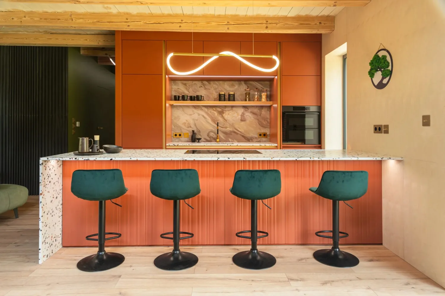 Photo of a built terracotta kitchen with a terrazzo island, green velvet bar stools and a wave pendant light